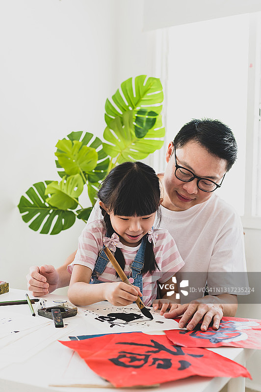 年轻亚裔中国女孩在客厅与父亲练习中国书法图片素材