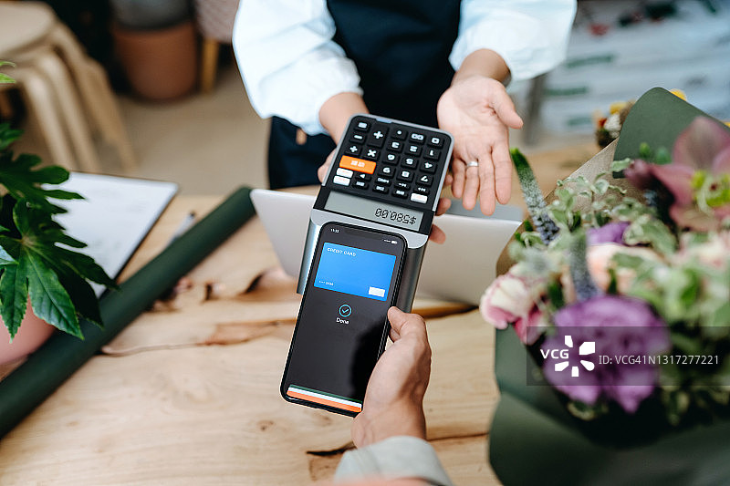 亚洲年轻男子在花店用手机支付购买鲜花（主观视角）：非接触式支付图片素材