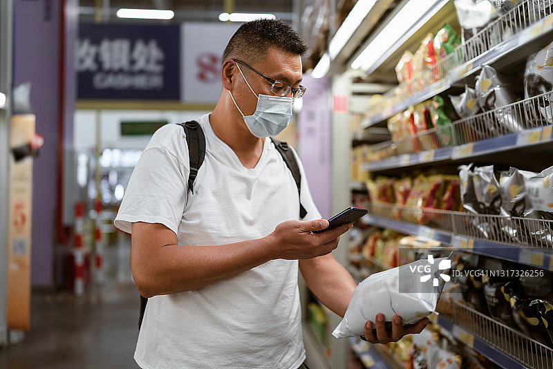 一位中年男子在超市购物，用手机扫描商品包装袋上的二维码图片素材