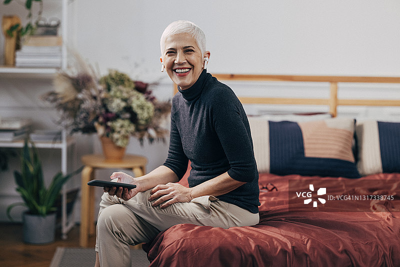微笑的老年妇女坐在床上使用手机图片素材