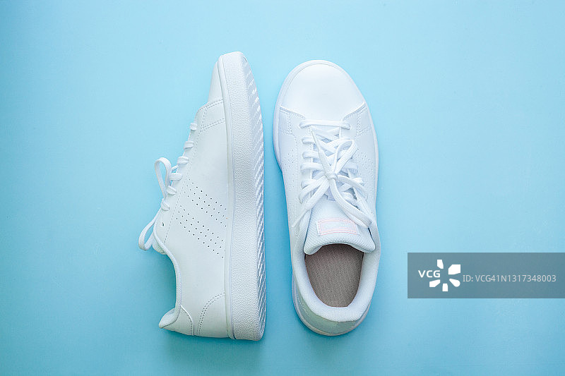 蓝色背景上的白色运动鞋，运动休闲服装风尚概念。夏季或春季时尚。图片素材
