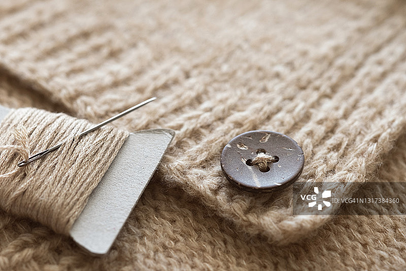针织毛衣、开衫或夹克上缝制精美的纽扣。靠近带针的线。女裁缝、家庭主妇或裁缝的职责和业务，特写。真实生活方式、爱好、手工制作的概念。图片素材