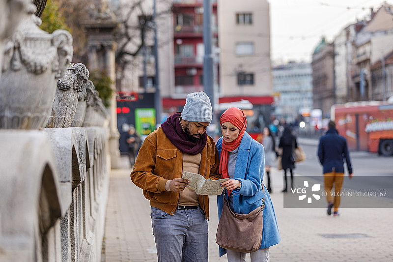 快乐的多民族夫妇走在街上，使用地图探索城市。图片素材
