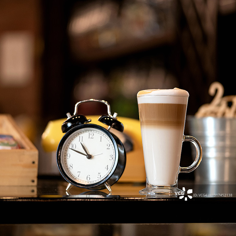 闹钟和玻璃杯拿铁咖啡饮品在桌子上，咖啡时间，早上好概念，柔焦，方形构图，图像顶部有复制空间图片素材