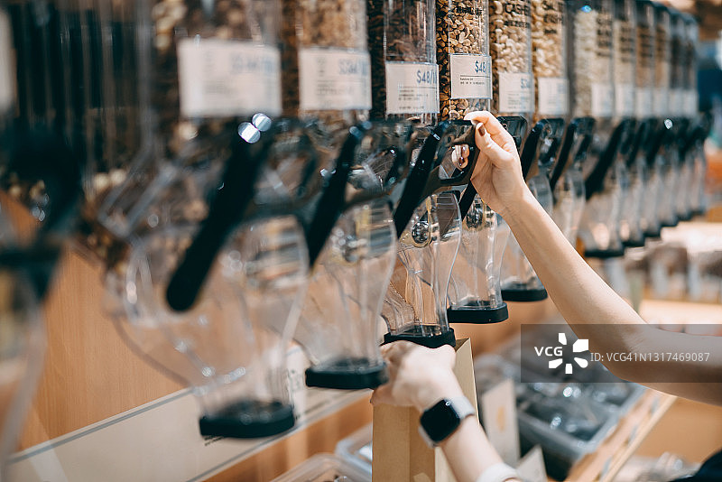 年轻的亚洲女性在无包装有机食品店购物，将坚果分装到纸袋中的特写。零浪费、无塑料、生态友好、绿色生活和可持续的生活方式图片素材