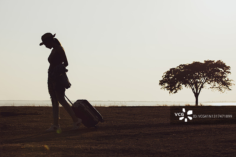 乡间小路上手提箱行走的女人剪影图片素材
