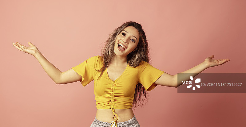 粉色背景前张开双臂欢笑的美丽年轻女人图片素材