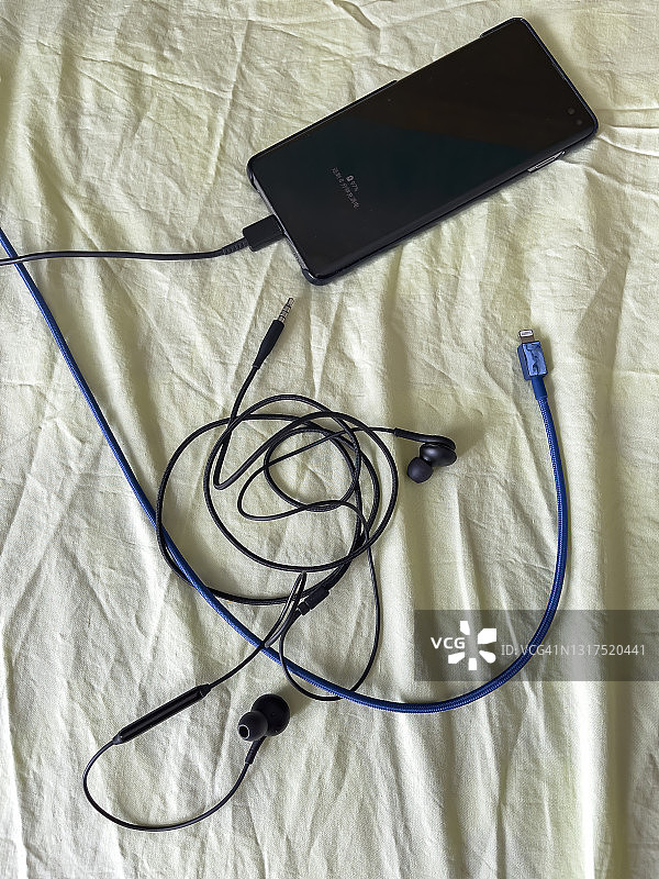 床上杂乱的手、耳机、充电线和耳机图片素材