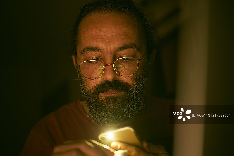 一个男人用手机灯光查看黑暗中的细节图片素材