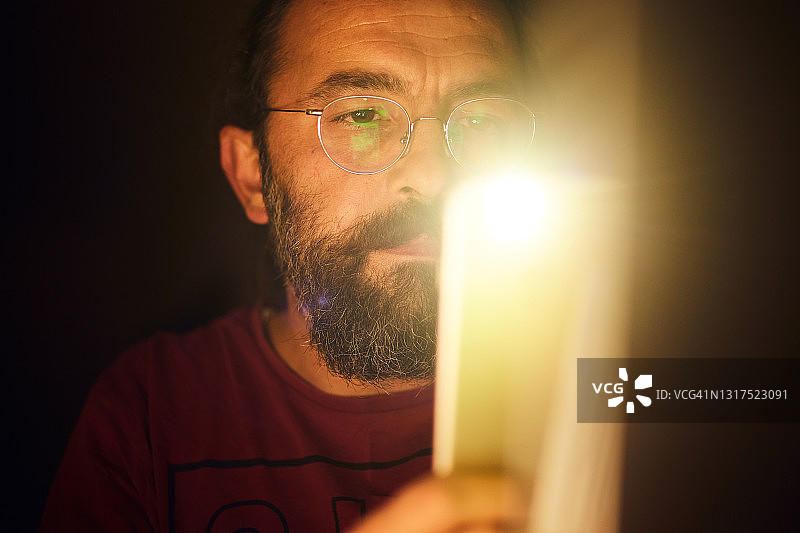 一个男人用手机灯光查看黑暗中的细节图片素材