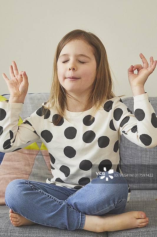 年轻女孩盘腿坐在沙发上做瑜伽图片素材