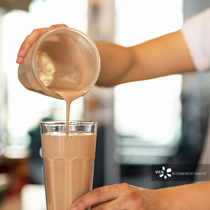 甜巧克力奶昔。厨师将鸡尾酒从摇壶倒入玻璃杯中，背景模糊，特写镜头。搅打软饮料，柔焦图片素材