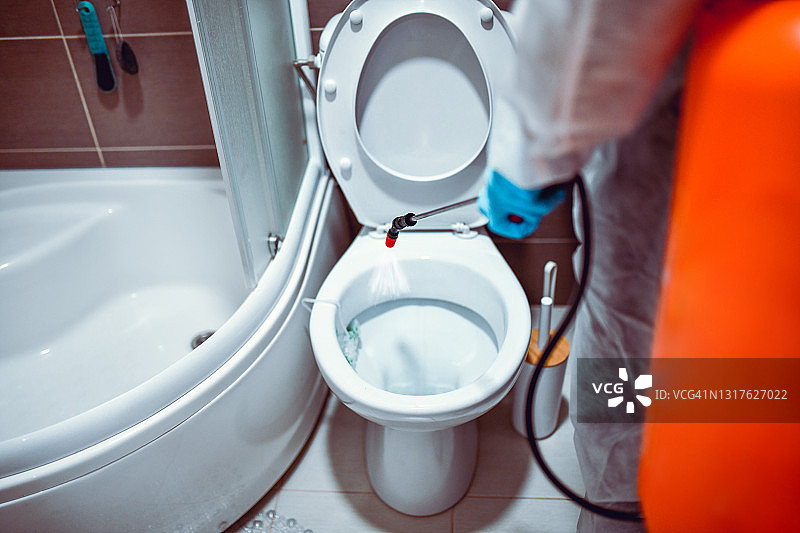 身穿防护服的医务人员对马桶座进行消毒，预防新冠肺炎图片素材