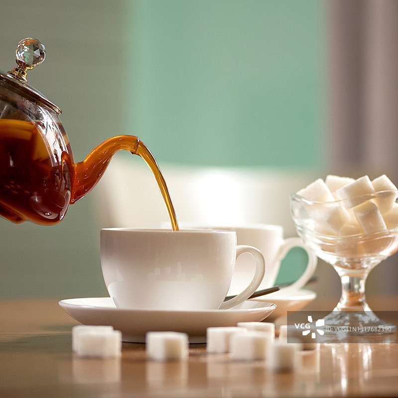 将热茶从透明茶壶倒入白色茶杯，木桌茶道图片素材