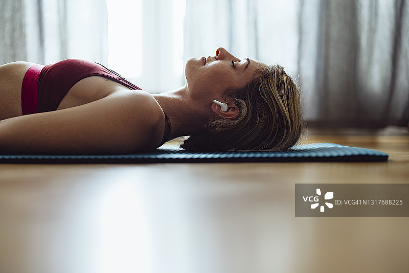戴着无线耳机在运动垫上冥想的女人图片素材