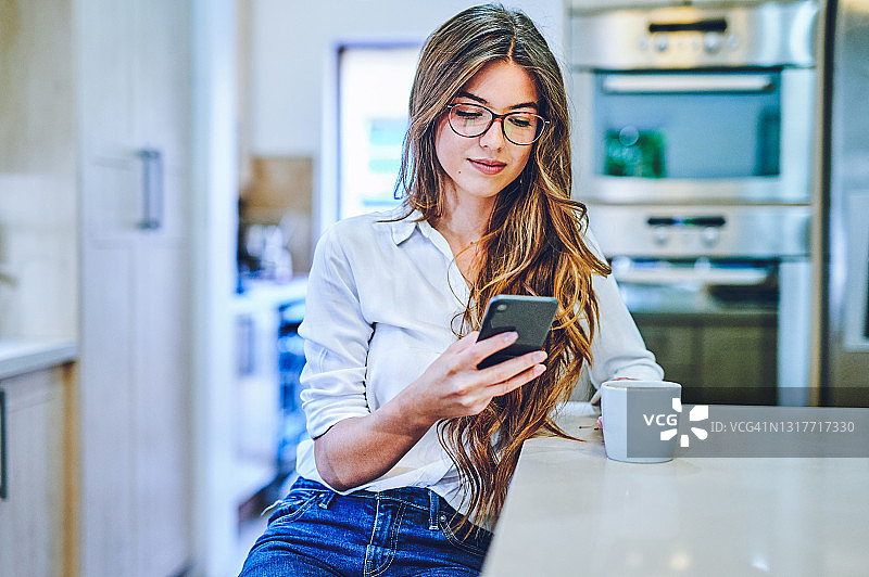 年轻女子在家喝咖啡玩智能手机图片素材
