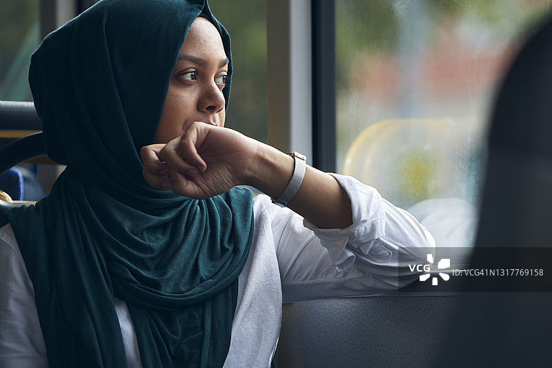 在公共汽车上，透过窗户向外看的年轻女子图片素材