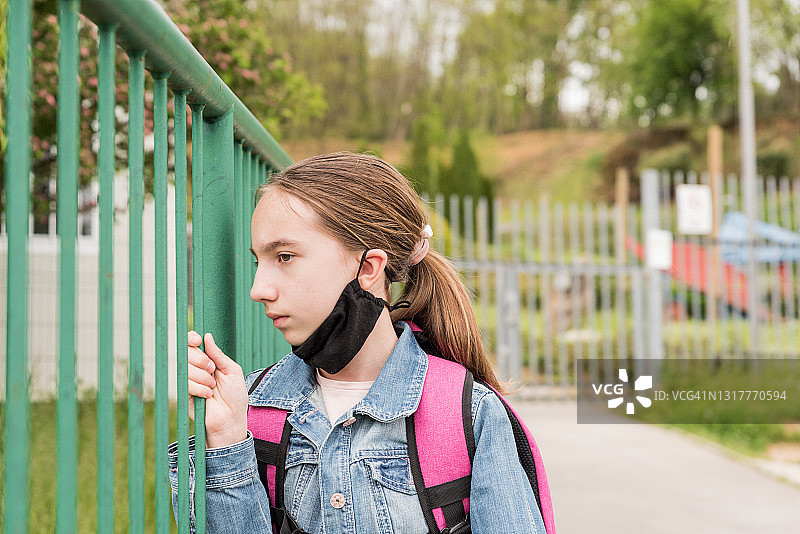 疫情封锁后等待学校重新开放的女学生，戴口罩站在学校围栏旁图片素材