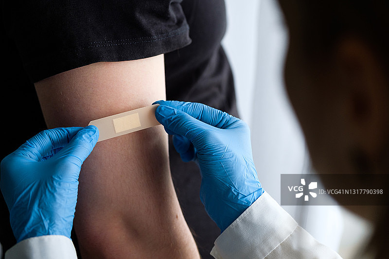 戴手套的医生或医疗专业人员在男人接种疫苗或注射药物后，在他的手臂上贴上贴片或胶带。医学和保健、疫苗接种和疾病治疗的概念。急救服务。图片素材