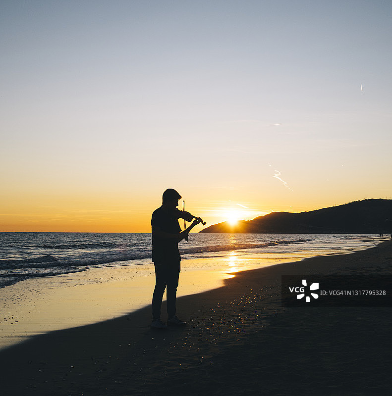 男孩在日落时分的海滩上拉小提琴图片素材