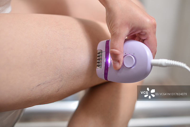 年轻女子在浴室用电动脱毛器脱毛特写图片素材