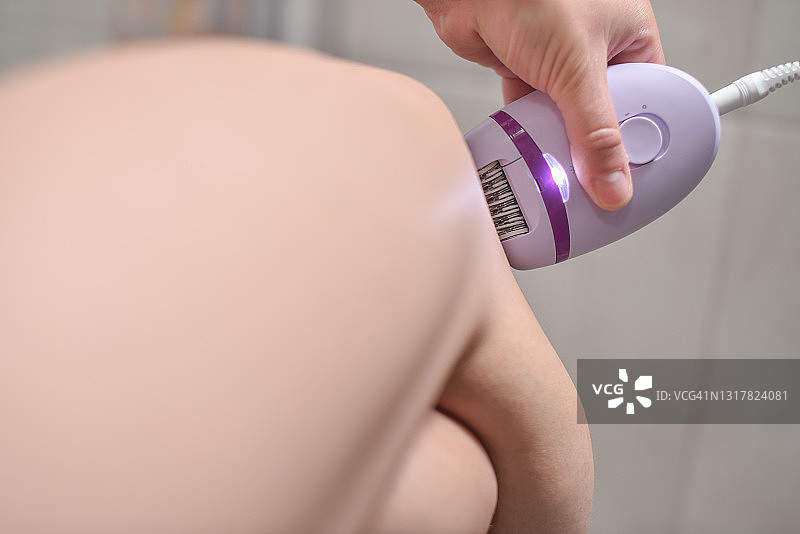 年轻女子在浴室用电动脱毛器脱毛特写图片素材