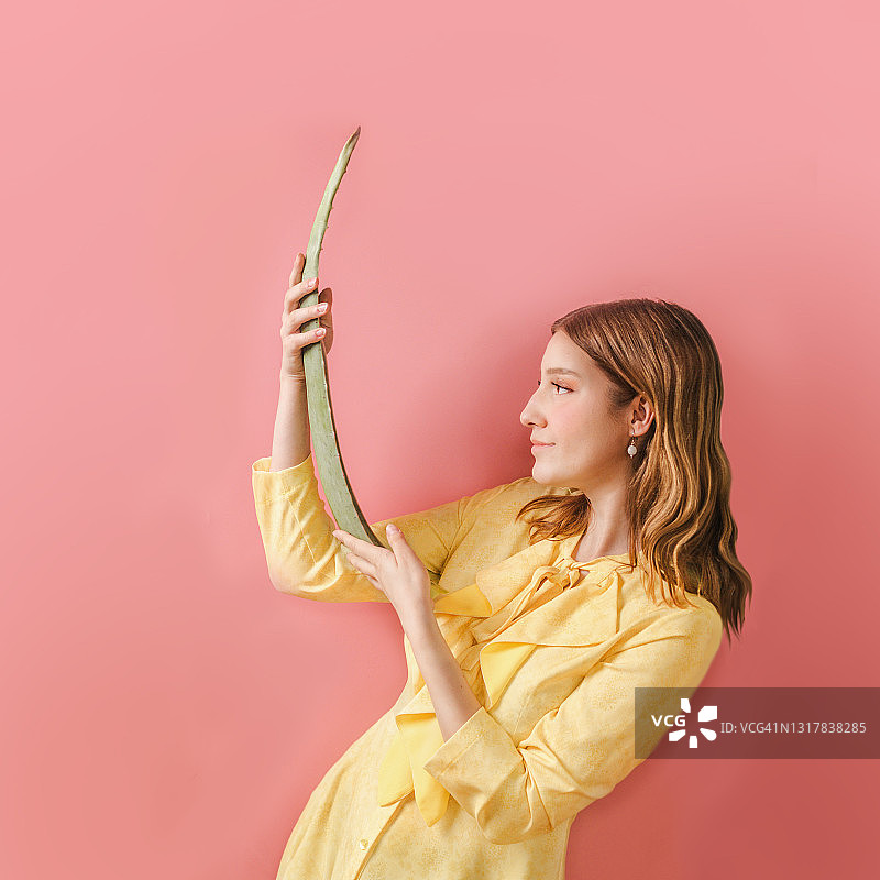 一位穿着黄色连衣裙的年轻女子手持芦荟叶图片素材