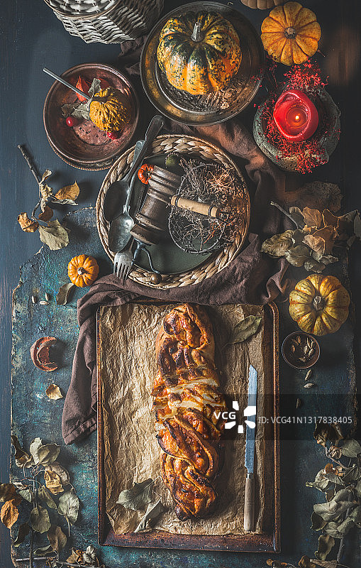 南瓜辫子蛋糕，秋叶，燃烧的蜡烛配料和复古厨房用具在黑暗的厨房桌子上图片素材