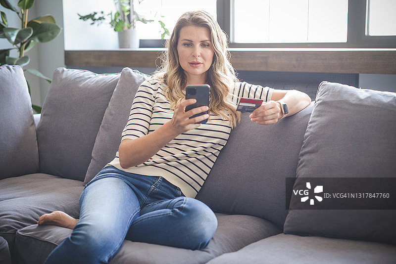 坐在沙发上的迷人中年妇女（网上购物，智能手机）图片素材