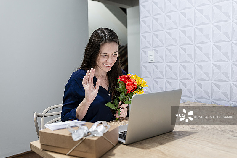 手捧鲜花和礼物的年轻女子通过视频通话感谢男友图片素材