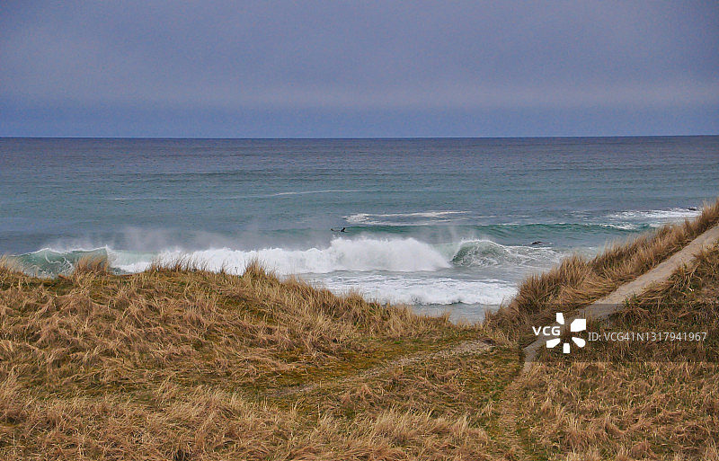 刮风天气里，海浪翻滚的海岸风光，有人尝试冲浪，傍晚的天空图片素材