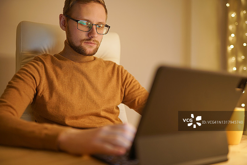 年轻男人坐在家里的桌子旁，用数位板工作图片素材