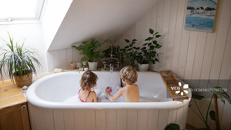 在家中浴室里，孩子们在泡泡浴中玩耍的背影图片素材
