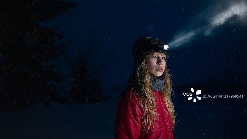 女孩戴着头灯站在雪夜的冬季户外图片素材