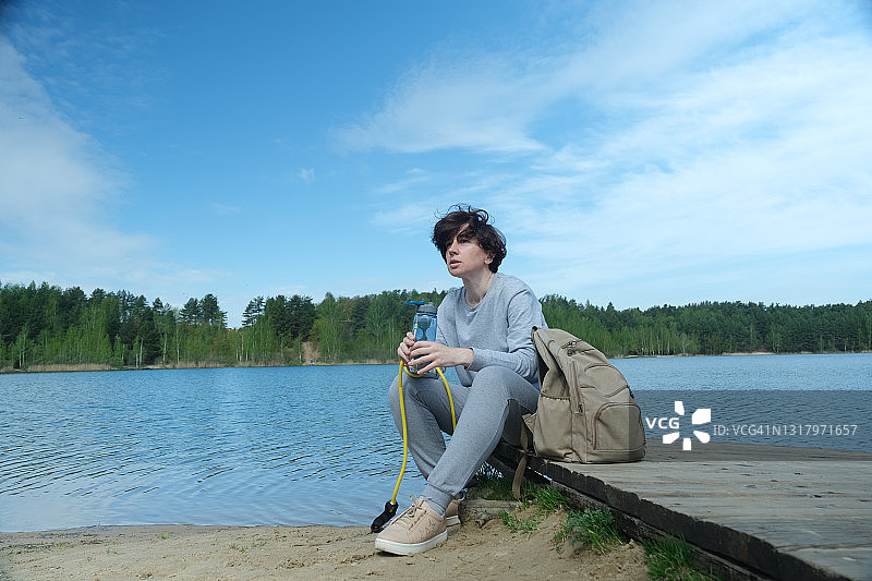 在湖岸用拉力带锻炼后喝水的中年妇女图片素材