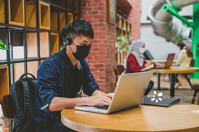戴口罩使用笔记本电脑的年轻亚洲商人图片素材