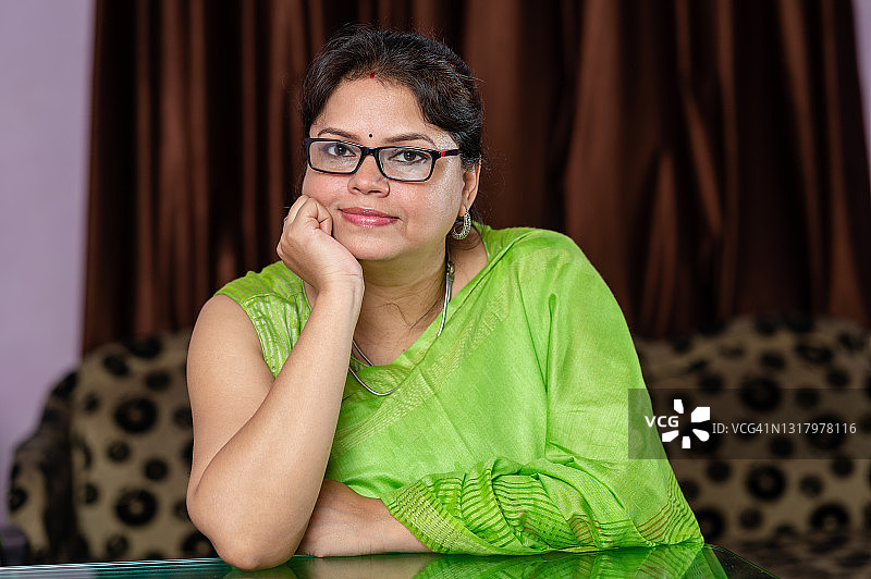 戴眼镜的快乐中年妇女坐在桌子和沙发旁图片素材