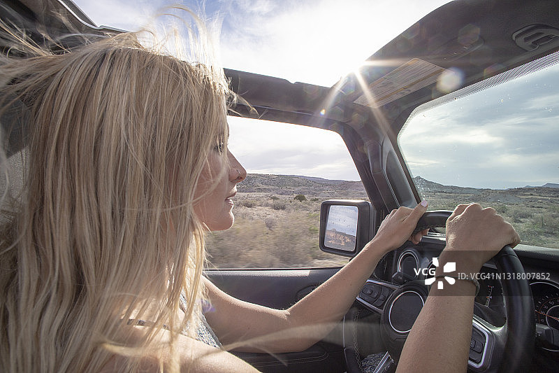 年轻女子驾驶越野车行驶在沙漠公路上图片素材