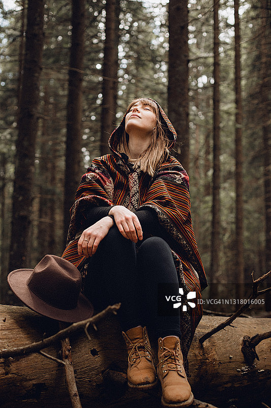 一位年轻漂亮的女子坐在树干上，享受着松树林中的自由图片素材