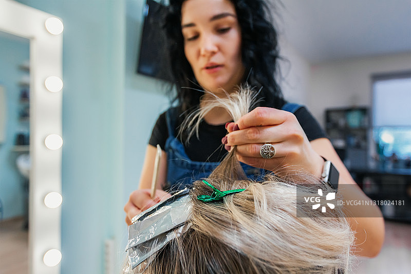 时尚发型师在挑染头发时，拿着一缕女性发型图片素材