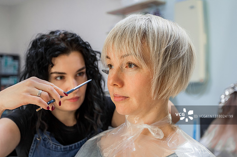 时尚女发型师在美发沙龙为年轻金发女人剪发图片素材