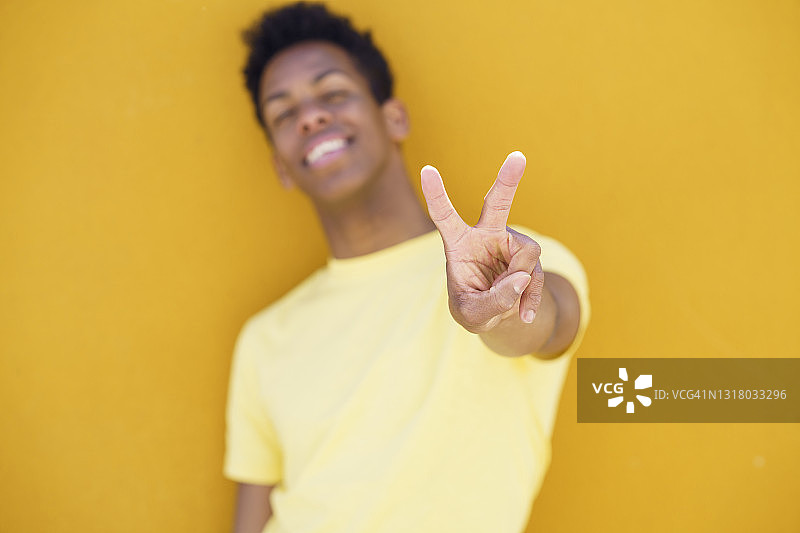 笑容满面的男人在黄色的墙壁前做出和平手势图片素材
