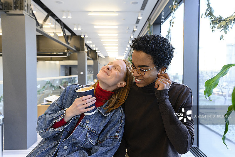 在咖啡馆里，快乐的女人靠在女性朋友的肩膀上图片素材