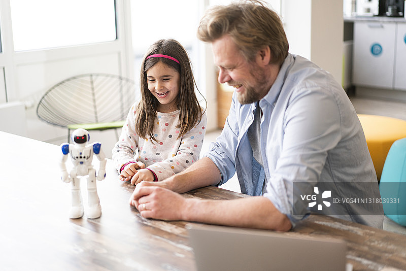 面带微笑的父女看着桌子上的机器人玩具图片素材