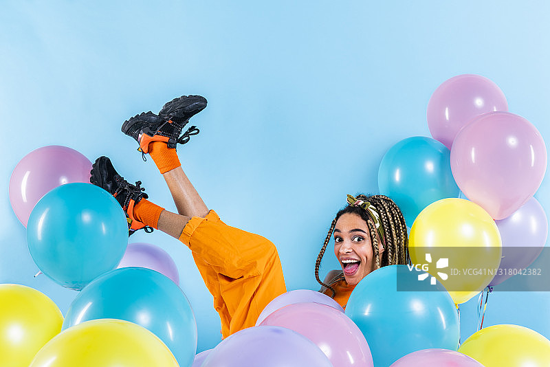 年轻女子在蓝色背景下的气球中抬起脚图片素材