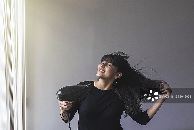 中年妇女在家使用吹风机时微笑图片素材