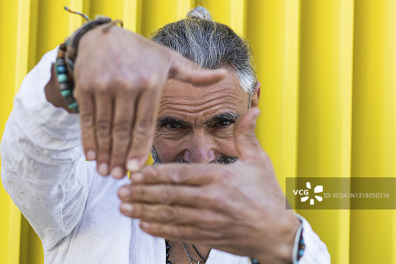 在墙壁前用手指取景的灰发男人图片素材