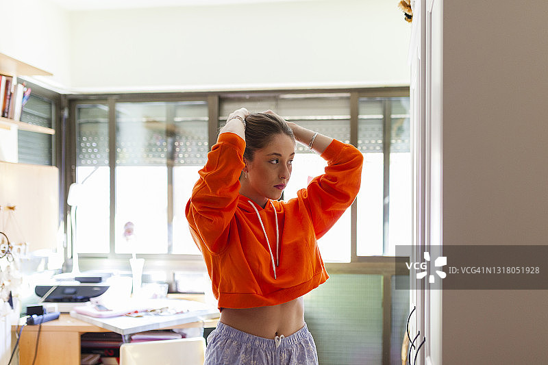 穿橙色露脐装在家照镜子的年轻女子图片素材