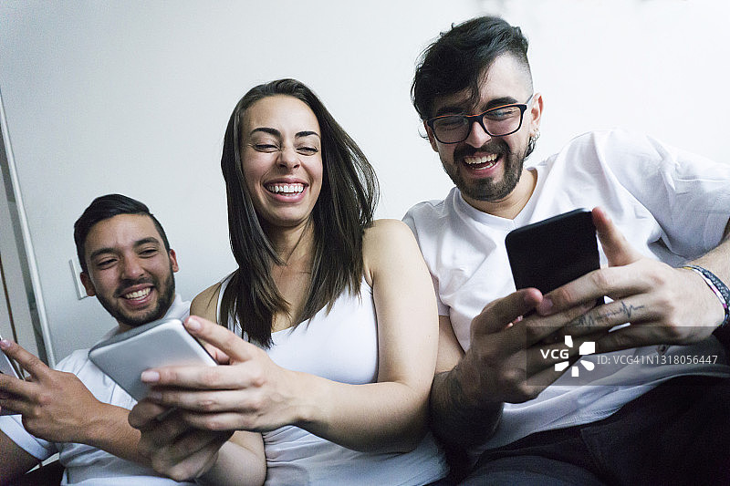 快乐的朋友们在看手机上的社交媒体时开怀大笑图片素材