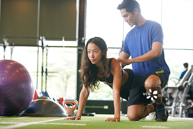 健身教练指导年轻女人在健身房做俯卧撑图片素材